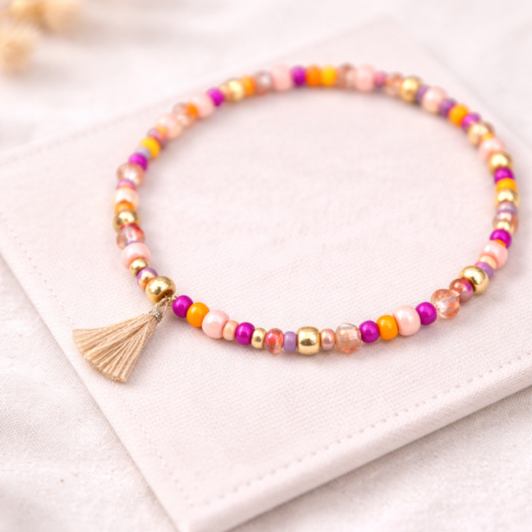 Buntes Perlenarmband mit pinken, orangefarbenen und rosé Perlen sowie goldenen Akzenten auf hellem Stoff – DIY Armband Set für kreative Projekte