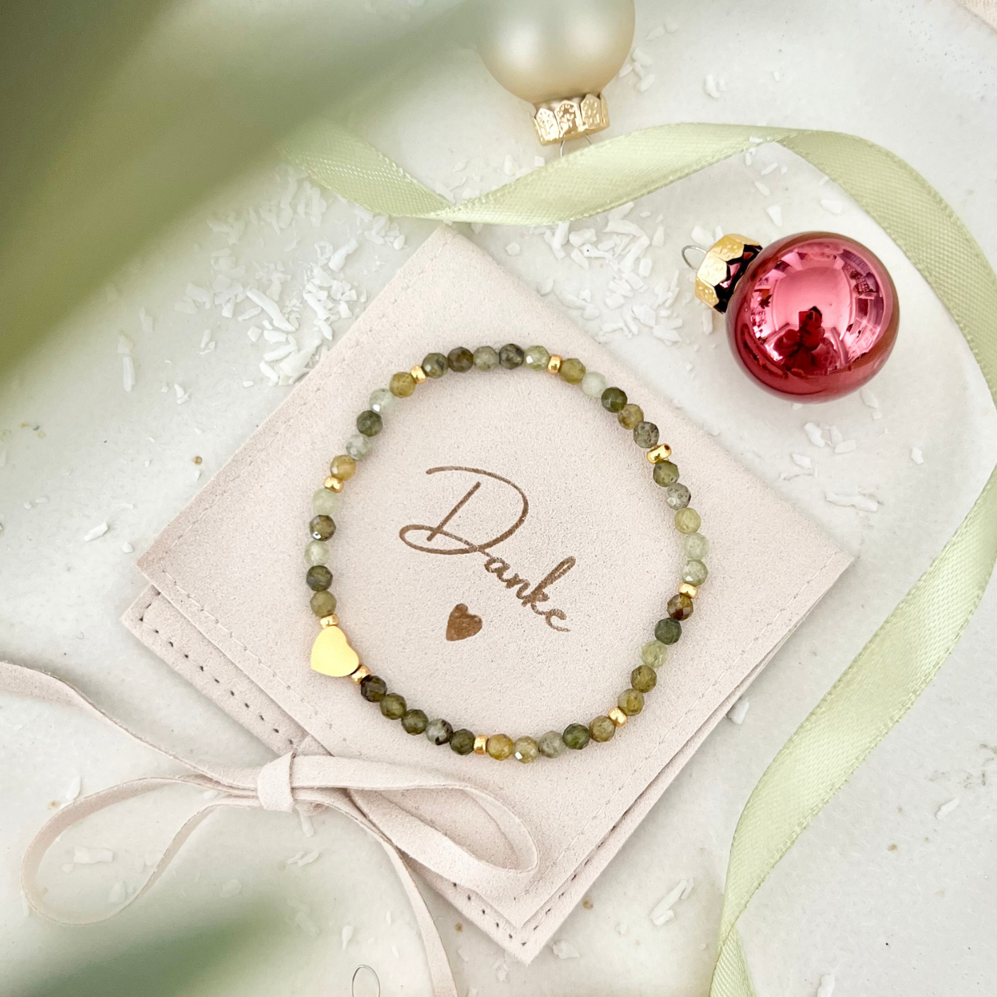Gesamtansicht des Armbands auf einem beigefarbenen Schmuckbeutel mit „Danke“-Schriftzug. Umgeben von Weihnachtskugeln, Schleifenband und Schneeflocken-Deko.