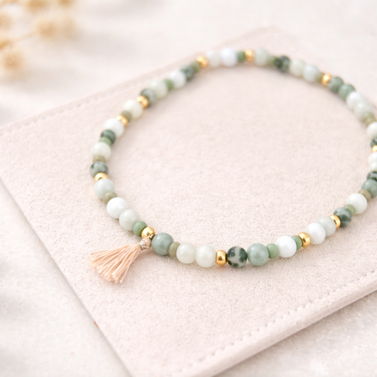 Perlenarmband in Grün- und Naturtönen mit goldenen Elementen und Quaste auf beigem Wildlederpad – DIY Armband basteln für Sommer Schmuck