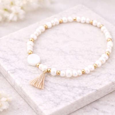 Weißes Perlenarmband mit goldenen Details und beigefarbener Quaste auf hellem Marmorstein – minimalistisches DIY Armband aus Perlenarmband Set