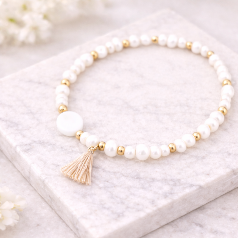 Weißes Perlenarmband mit goldenen Details und beigefarbener Quaste auf hellem Marmorstein – minimalistisches DIY Armband aus Perlenarmband Set