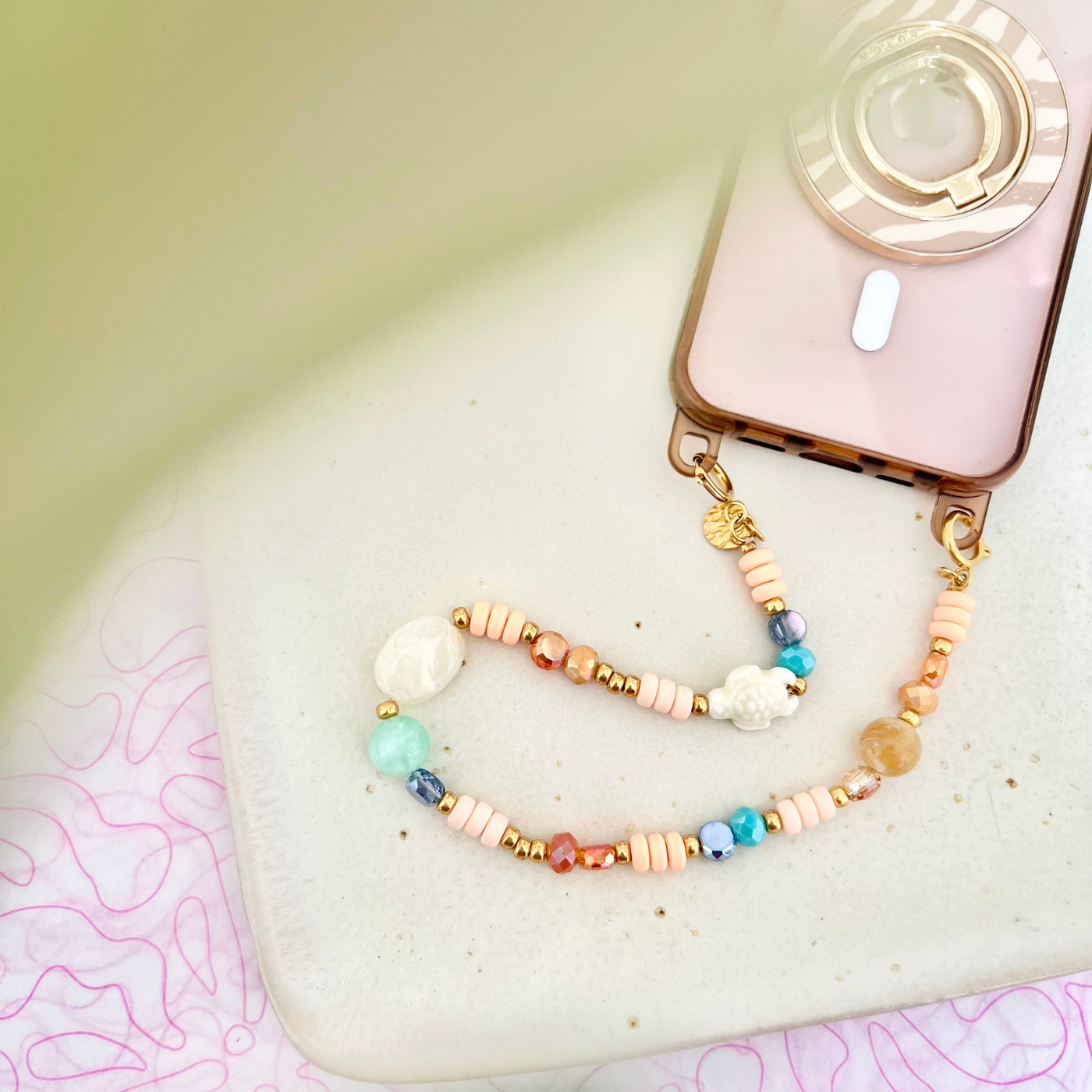 Smartphone mit transparenter Handyhülle und befestigter Perlen-Handykette LAGUNA mit Keramik-Schildkröte – praktisches Phone Strap Accessoire.