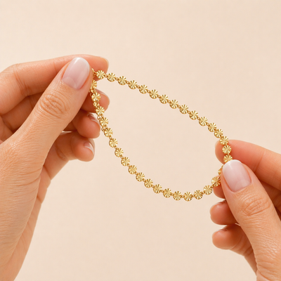 Goldenes Edelstahl Armband mit feinen Sonnen-Details wird zwischen zwei Fingern mit Babyboomer Maniküre gehalten, filigraner Damenschmuck, wasserfest und elegant