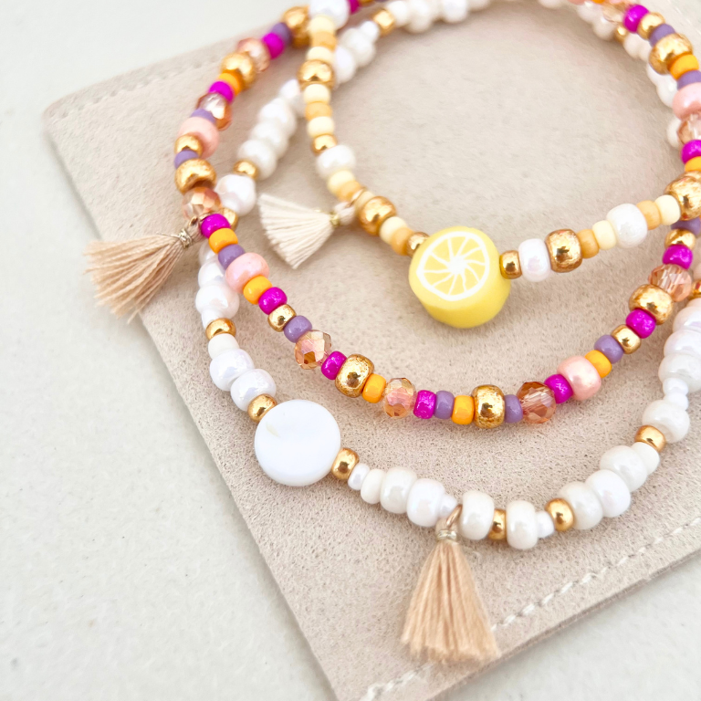 Detailaufnahme von mehreren Perlenarmbändern mit Naturstein-, Glas- und Süßwasserperlen in verschiedenen Farben auf beigem Untergrund – DIY Schmuckset für Armbänder