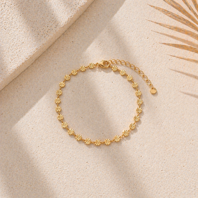 Goldenes Edelstahl Armband mit kleinen Sonnen-Elementen, filigranes Design auf hellem Stein platziert, wasserfestes Schmuckstück für Damen im minimalistischen Stil