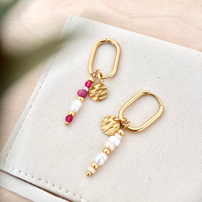 Zwei goldene Ohrringe mit unterschiedlichen Perlenanhängern in Rosa und Grün auf hellem Untergrund, minimalistisches Schmuckbild mit Farbvarianten