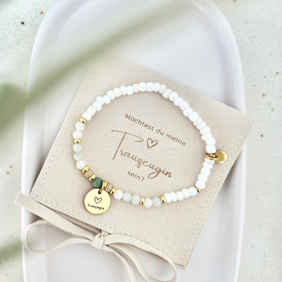 Handgemachtes Armband aus weißen Perlen mit goldenen Akzenten, grünem Detail und graviertem Anhänger „Trauzeugin“, auf beigem Schmuckkärtchen mit der Aufschrift „Möchtest du meine Trauzeugin sein?“