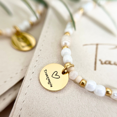 Nahaufnahme eines eleganten Armbands aus echten Süßwasserperlen und goldfarbenem Edelstahlanhänger mit Herz und Schriftzug „Trauzeugin“ – stilvolles Freundschaftsarmband für Hochzeit oder Verlobung
