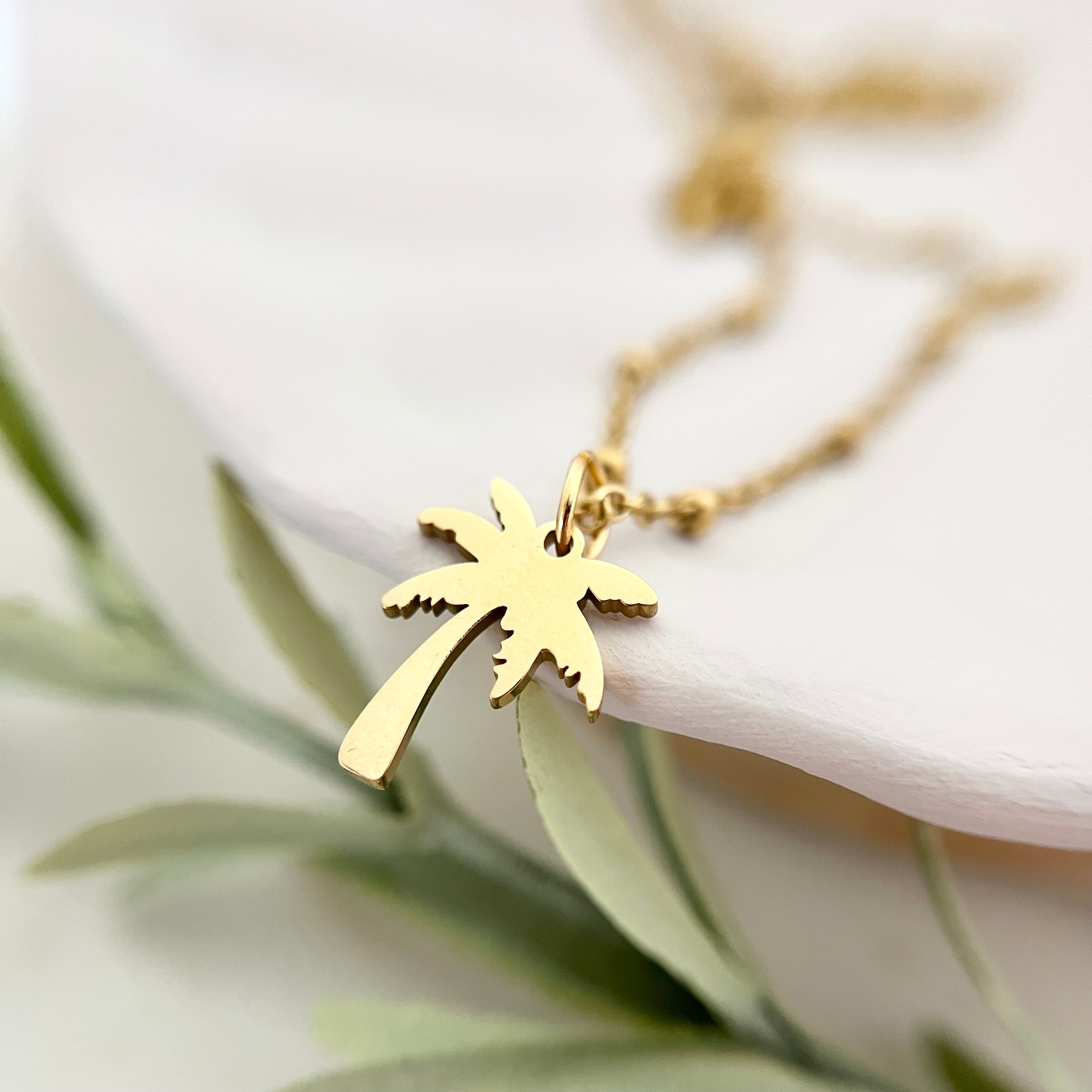 Nahaufnahme des goldenen Palmenanhängers der Kette PALMERA, der tropisches Urlaubsgefühl und Sommerflair verleiht.
