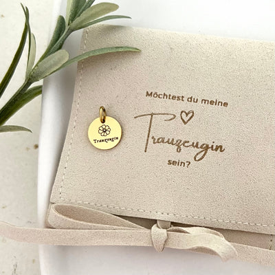 Topshot vom goldenen Anhänger mit der Gravur "Trauzeugin" und Tasche mit der Aufschrift „Möchtest du meine Trauzeugin sein?“ – besondere Einladung zur Trauzeugin.