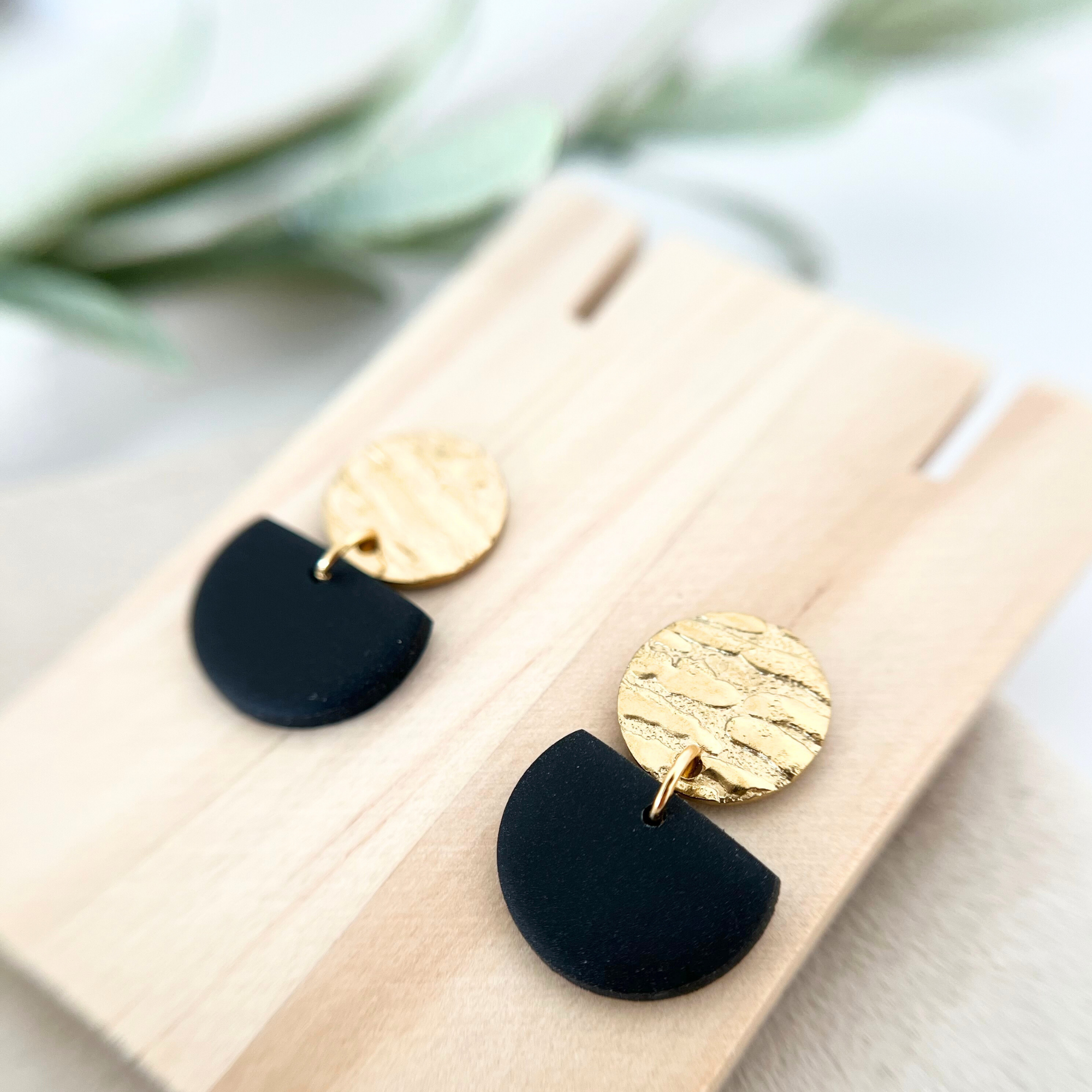 Ein Paar handgemachte schwarze Ohrringe MURADA aus Edelstahl und Polymer Clay, auf einem Holzstück präsentiert, in eleganter Halbkreis-Form