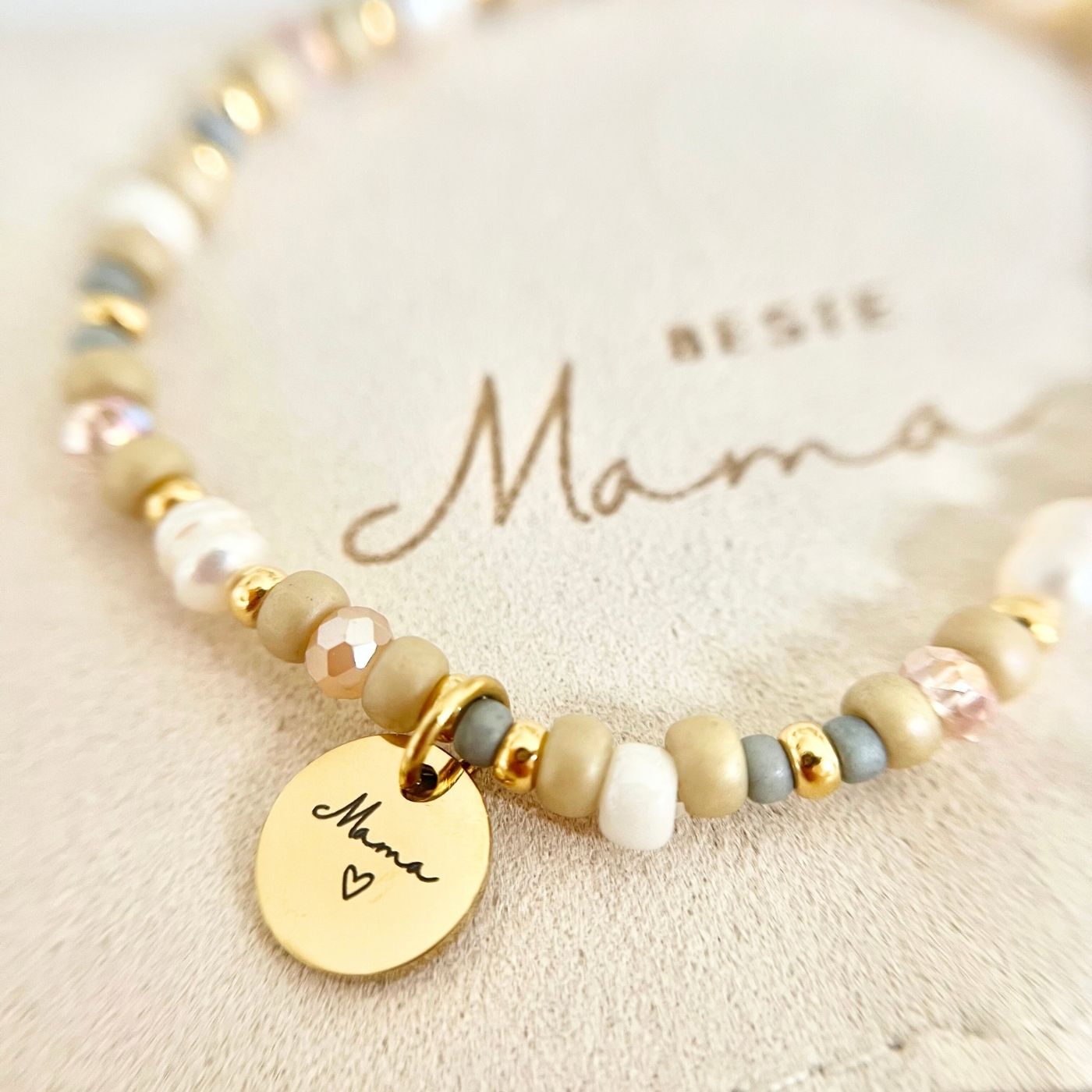 Nahaufnahme des Gravur-Anhängers „Mama“ mit Herz, eingerahmt von facettierten Glasperlen, Miyuki-Perlen und Süßwasserperlen in hellen Beige- und Roséfarben.