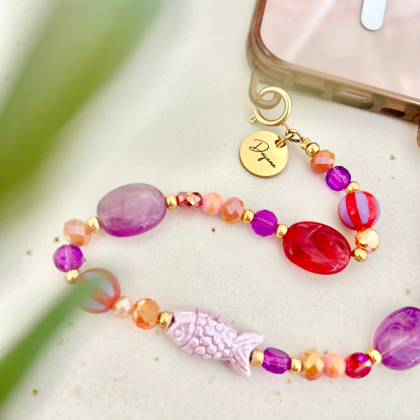 Smartphone mit transparenter Handyhülle und befestigter personalisierter Handykette aus bunten Perlen – dekoratives Handyband mit graviertem Namensanhänger.