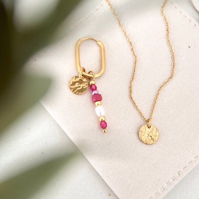 Goldener Ohrring mit rosa und weißen Perlen neben passender Kette auf hellem Schmuckbeutel, minimalistisches Produktbild in warmen Naturtönen