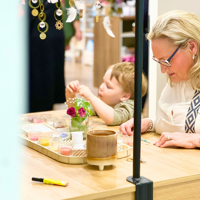 Kind bastelt konzentriert ein Perlenarmband gemeinsam mit seiner Oma beim Mini-Me Schmuck Workshop – kreative Auszeit an einem liebevoll dekorierten Basteltisch in Wuppertal