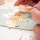 Nahaufnahme beim Ausstechen von quadratischen Anhängern aus mintgrüner Polymer Clay Modelliermasse mit 23 Karat Blattgold – kreativer Arbeitsschritt im Schmuck Workshop in Wuppertal zum DIY Schmuck selber machen