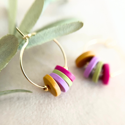 Detailaufnahme einer goldfarbenen Creole HOOPS, die mit bunten Polymer Clay-Anhängern für einen spielerischen Touch kombiniert wurde