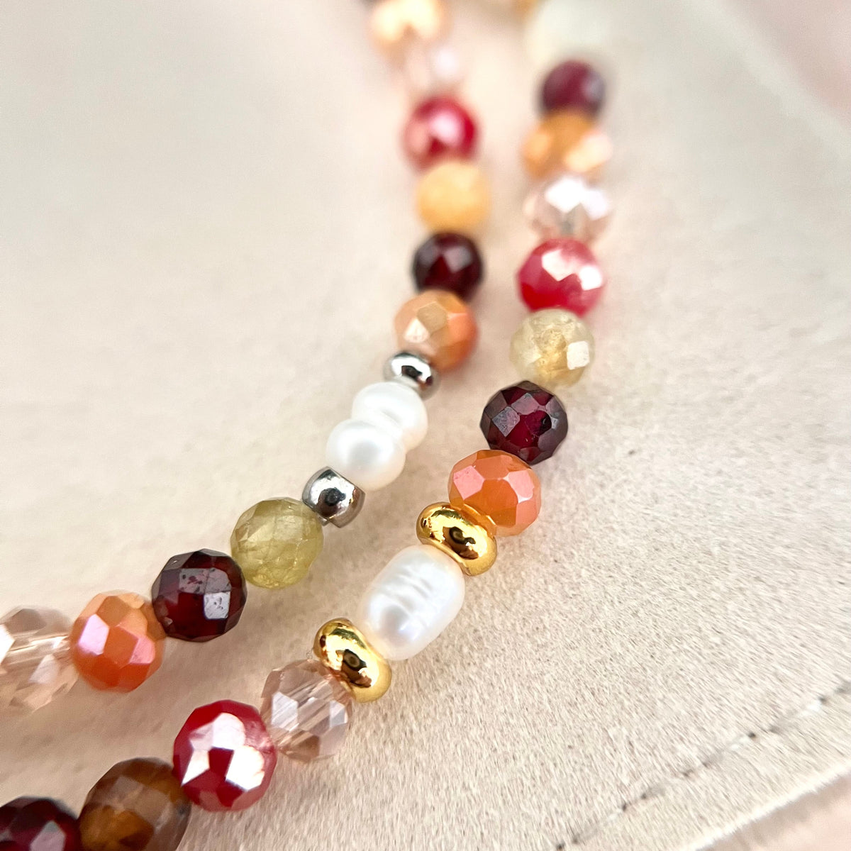 Detailaufnahme des weihnachtlichen Armbands NOELLE von ROSEMARY & Olive mit facettierten Naturstein- und Glasperlen in Weinrot, Rot, Apricot und Grün. Weiße Süßwasserperlen und glänzende goldene Akzente ergänzen das handgefertigte Perlenarmband auf einem cremefarbenen Schmuckbeutel.