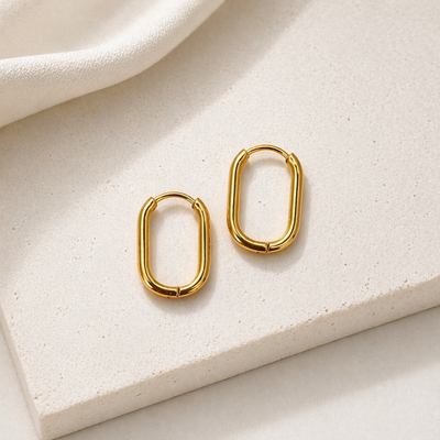 Goldene Huggie Hoops Creolen aus Edelstahl auf hellem Stein, ovale kleine Ohrringe, wasserfester minimalistischer Schmuck