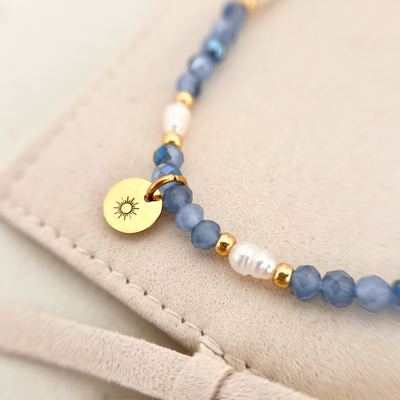 Detailaufnahme eines Perlenarmbands mit blauen Facettenperlen, weißen Süßwasserperlen und goldenen Elementen, filigraner Damenschmuck mit Sonnenanhänger