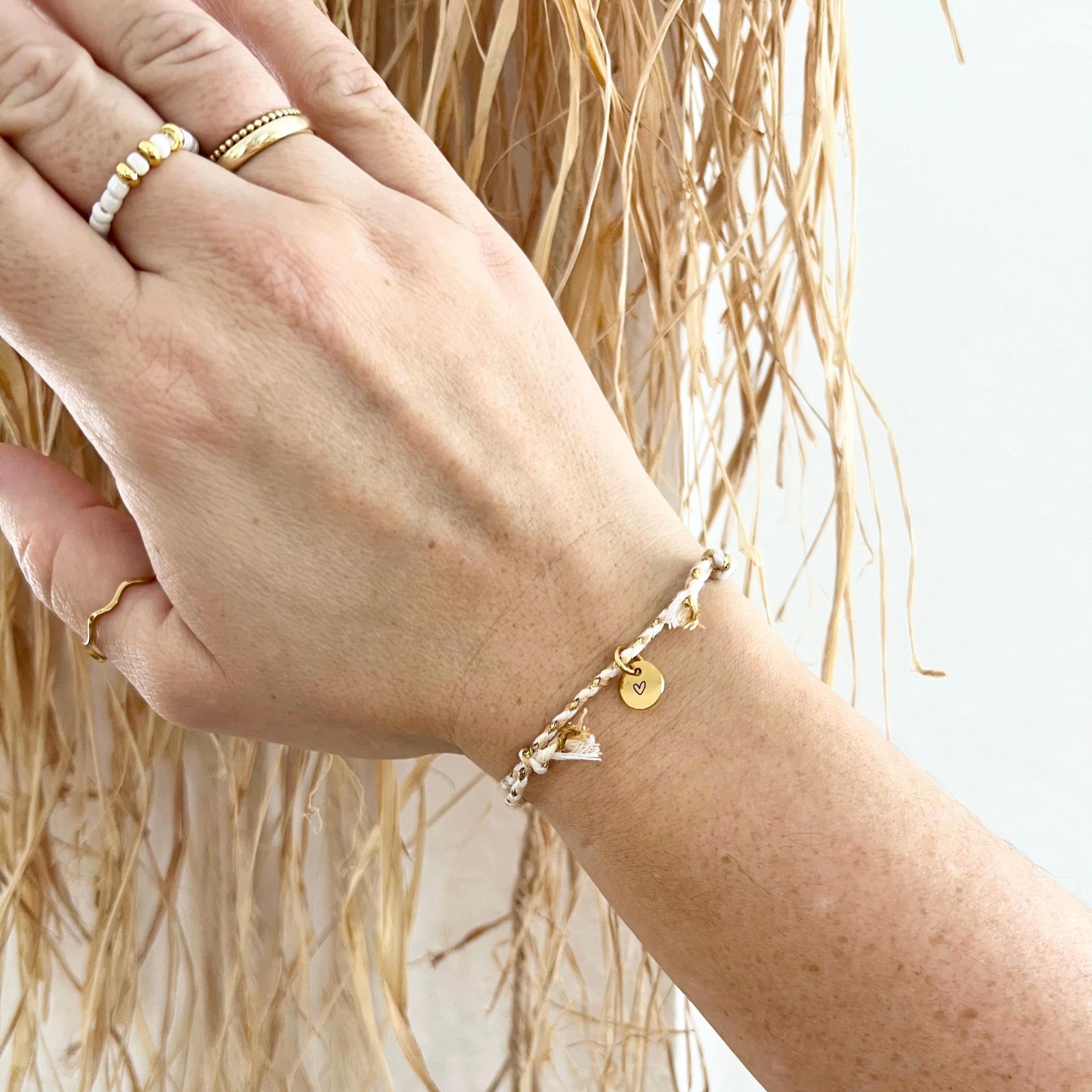 Armband VINYOLA getragen am Handgelenk, zeigt die zarte Baumwollkordel und den goldenen Herzgravur-Anhänger