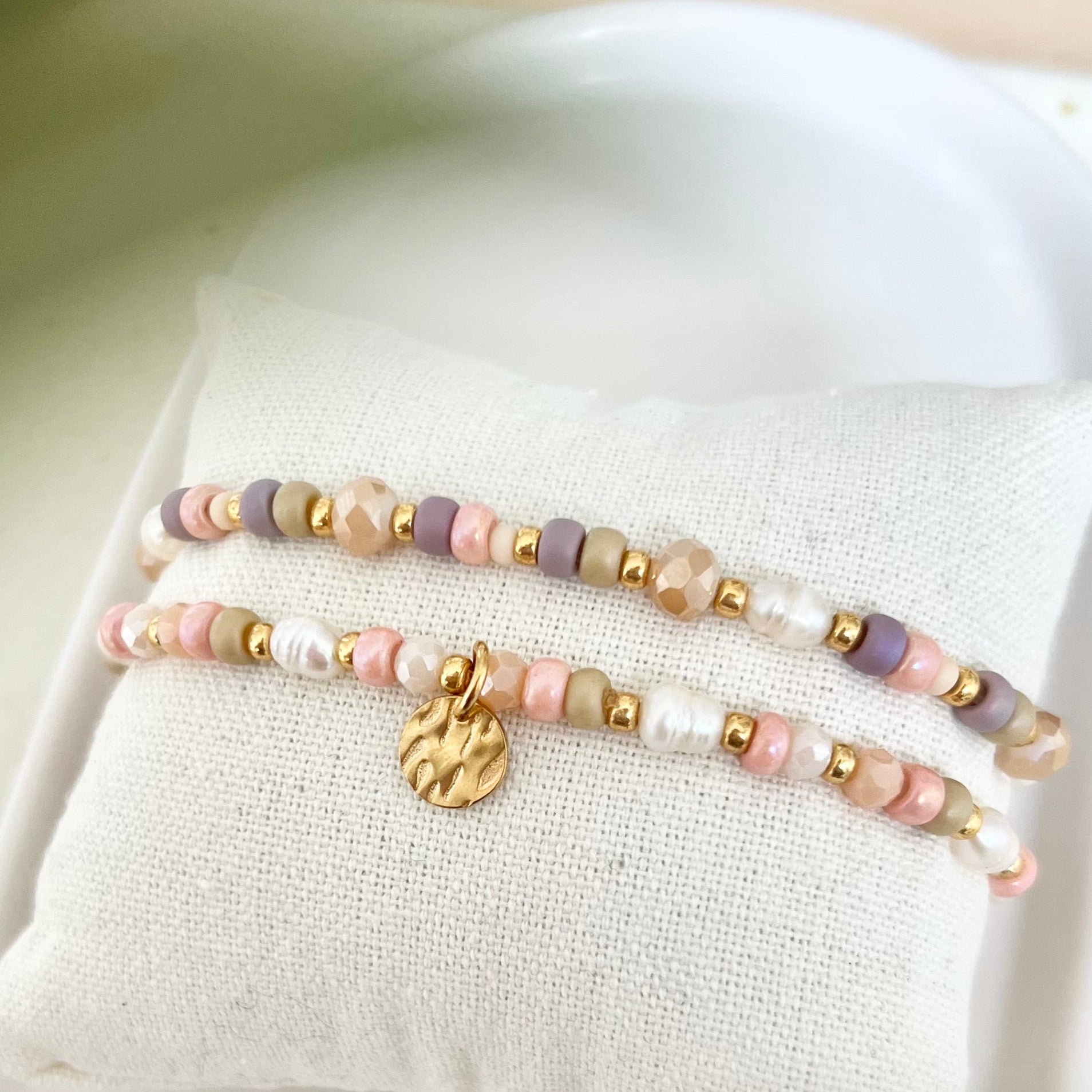 Zartes Armband in Rosa-, Beige- und Weißtönen mit goldenen Details, auf weichem Stoff arrangiert, natürliches Licht und weiche Schatten.