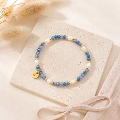 Blaues Perlenarmband mit kleinen Perlen und goldenem Sonnenanhänger aus Edelstahl auf hellem Stein platziert, wasserfestes Schmuckstück für Frauen im sommerlichen Stil