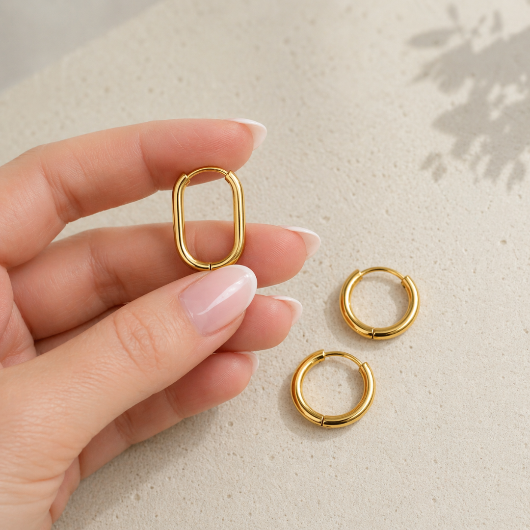 Goldene Huggie Hoops Creole aus Edelstahl wird in der Hand gehalten, daneben zwei runde kleine Creolen, Mix & Match Ohrringe für Damen