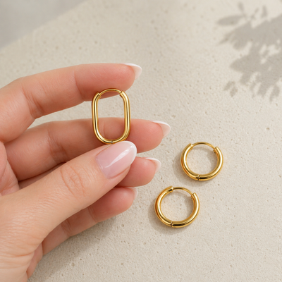 Goldene Huggie Hoops Creole aus Edelstahl wird in der Hand gehalten, daneben zwei runde kleine Creolen, Mix & Match Ohrringe für Damen