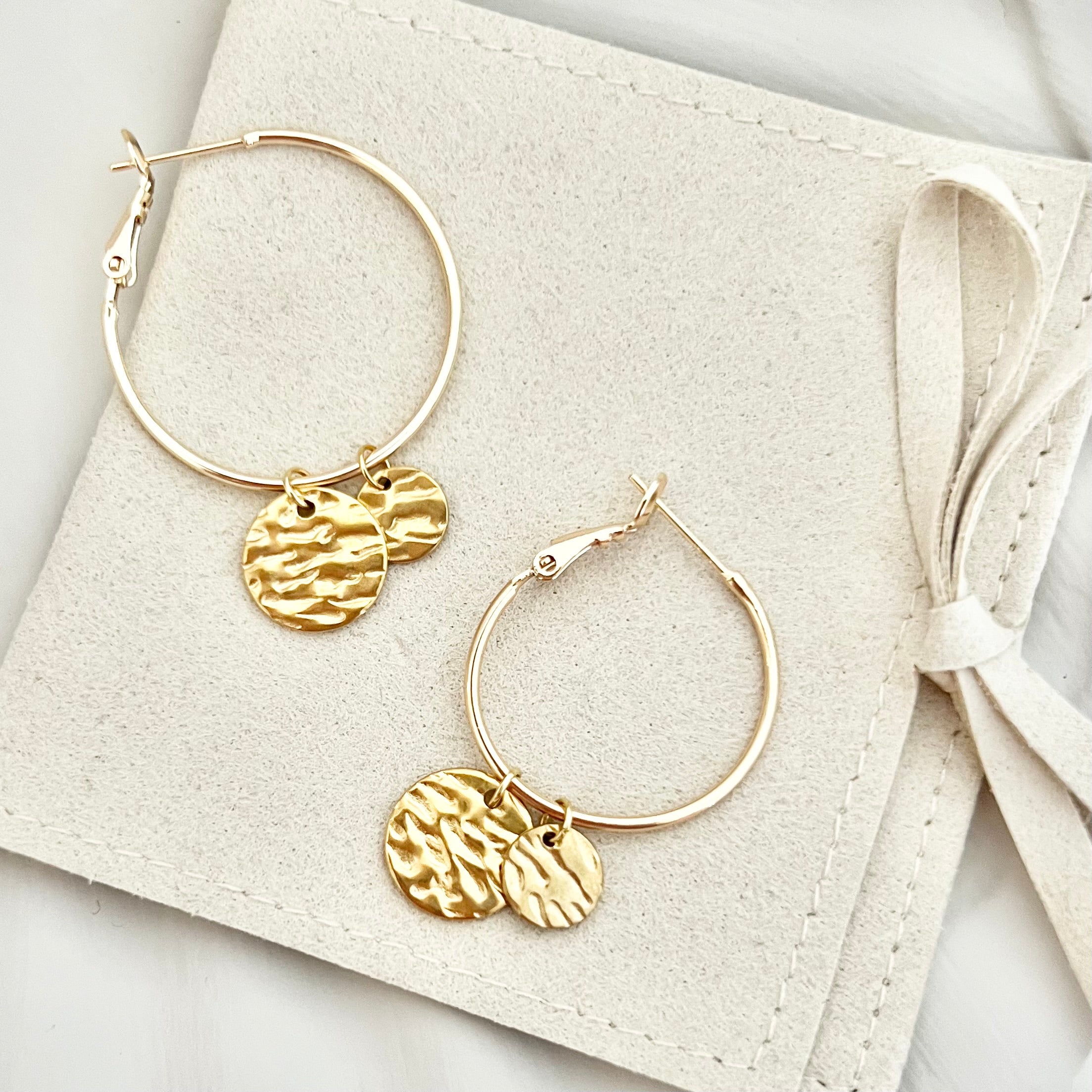 Paar goldene Creolen Ohrringe CASA aus Edelstahl, auf einer Tasche drapiert, um das klassische Design und die glänzende Oberfläche zu zeigen.