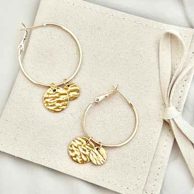 Paar goldene Creolen Ohrringe CASA aus Edelstahl, auf einer Tasche drapiert, um das klassische Design und die glänzende Oberfläche zu zeigen.