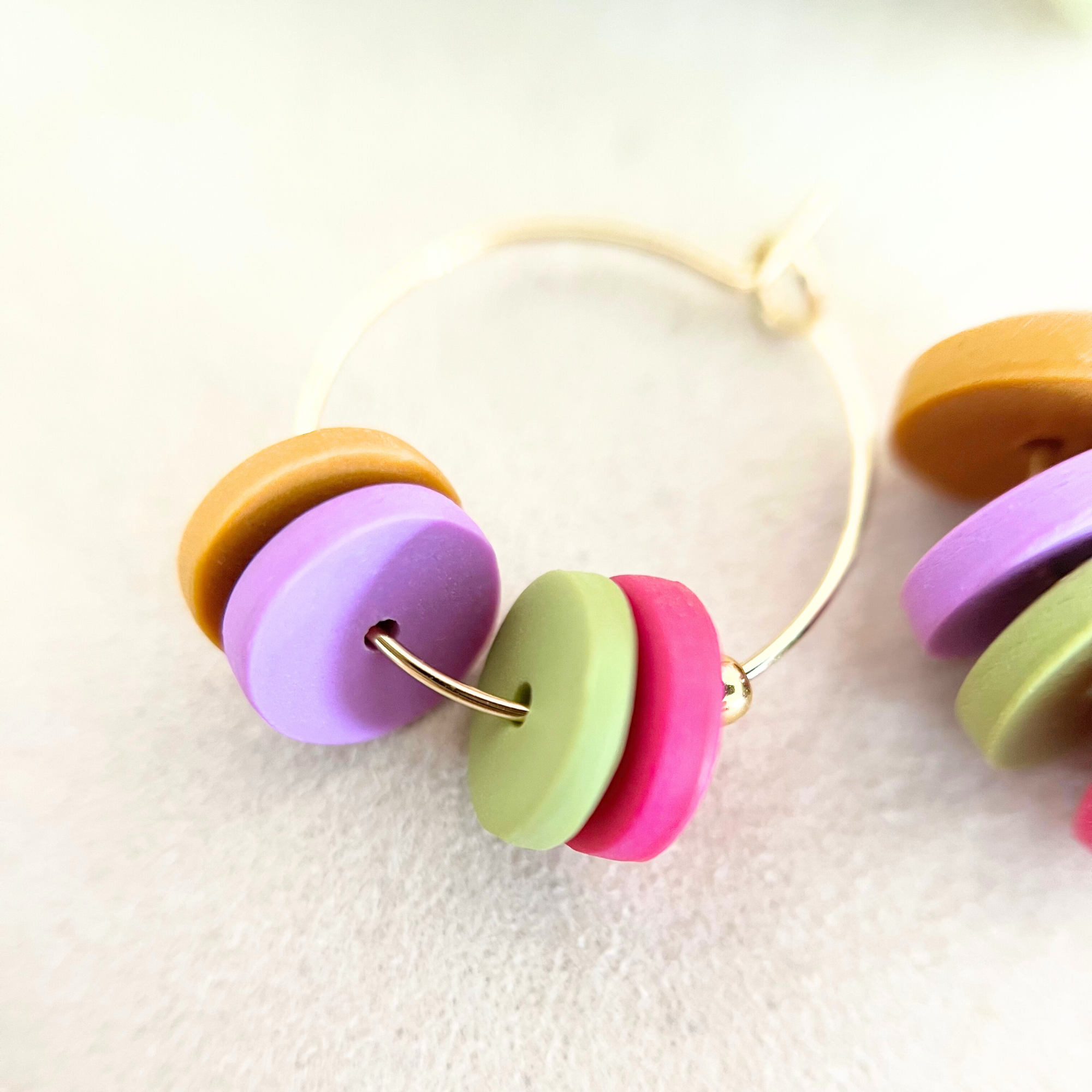 Nahaufnahme einer goldfarbenen Creole HOOPS, die aus Edelstahl gefertigt ist und farbenfrohe Polymer Clay-Anhänger aufweist, für einen lebendigen Akzent