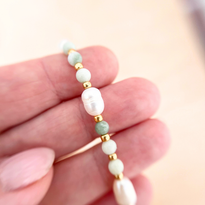 Hand hält eine feine Perlenkette mit Natursteinperlen in Grün und echter Süßwasserperle, goldene Akzente sichtbar, hochwertige Verarbeitung im Detail