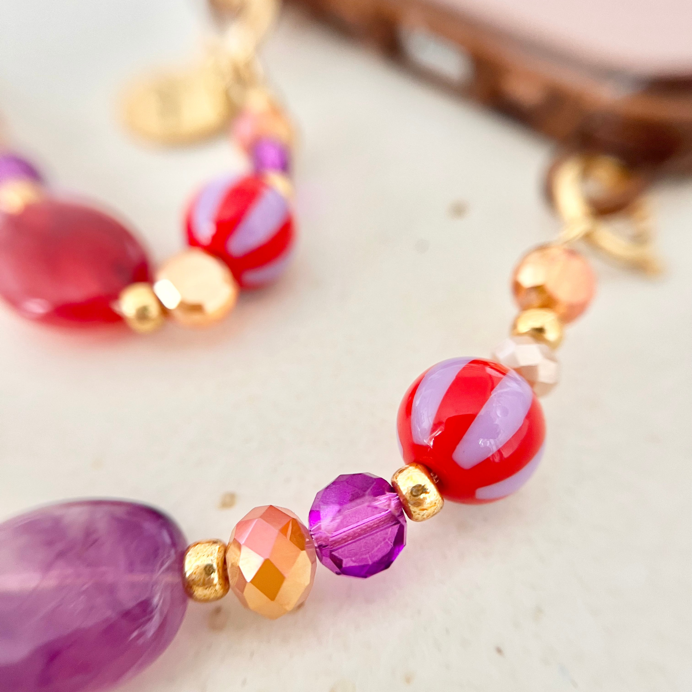 Detailaufnahme einer roten und lilafarbenen Perlenkombination mit facettierten Glasperlen und goldenen Zwischenperlen – hochwertige Handykette als Handyband.