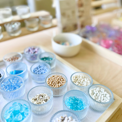 Verschiedene Perlen in zarten Blau-, Beige- und Naturtönen, sortiert in kleinen Glasschalen auf einem weißen Tablett. Die liebevoll präsentierte Auswahl ist Teil des DIY Schmuck Workshops bei Rosemary & Olive in Wuppertal – ideal zum Gestalten von Armbändern, Ketten und Ohrringen im kreativen Perlen Workshop
