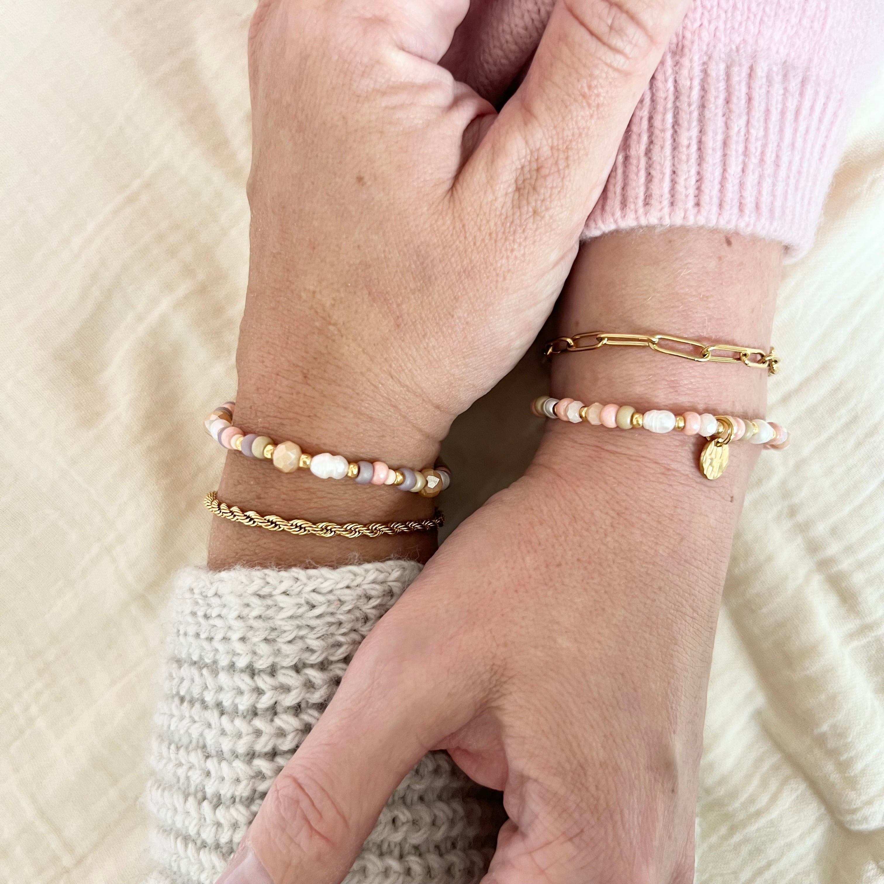 Zwei Hände tragen ähnliche Armbänder in Pastellfarben mit goldenen Details und Süßwasserperlen. Symbol für Freundschaft und Zusammenhalt.