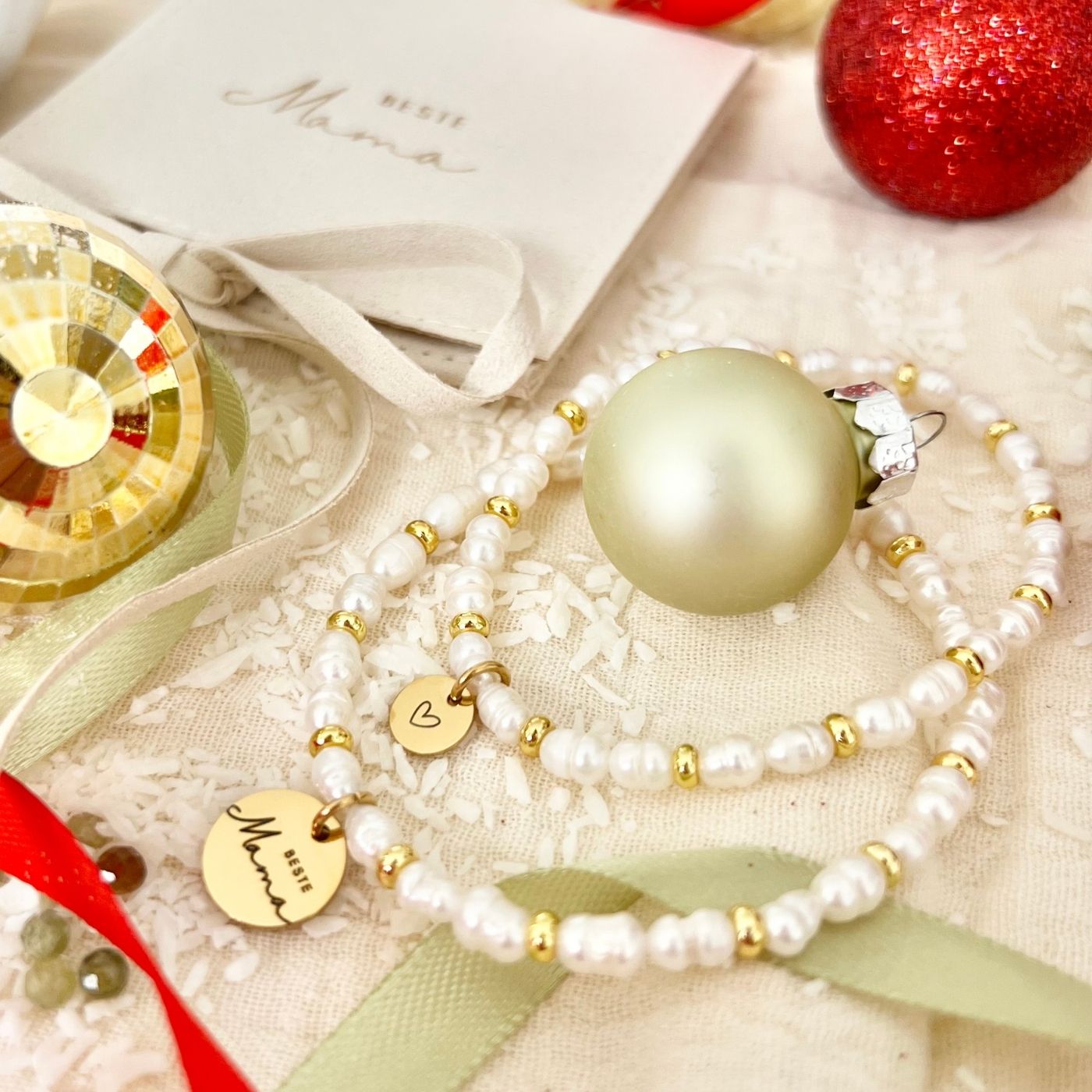 Armband aus weißen Süßwasserperlen mit goldenen Elementen und Herz-Anhänger, präsentiert auf Schmucktäschchen „Beste Mama“.