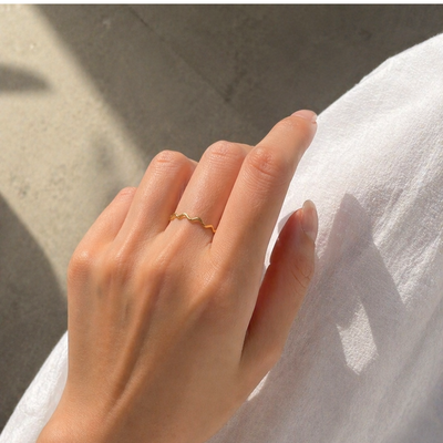 Goldener Wellenring aus Edelstahl am Finger getragen, warmes Licht, natürliche Hautstruktur, minimalistischer Schmuck in neutralen Farben