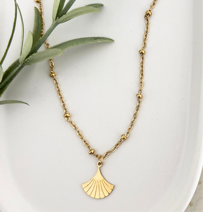 Goldene Edelstahlkette DEIA auf einem weißen Tablet, der Ginkgo-Blatt Anhänger wird gezeigt, der das elegante Design unterstreicht.
