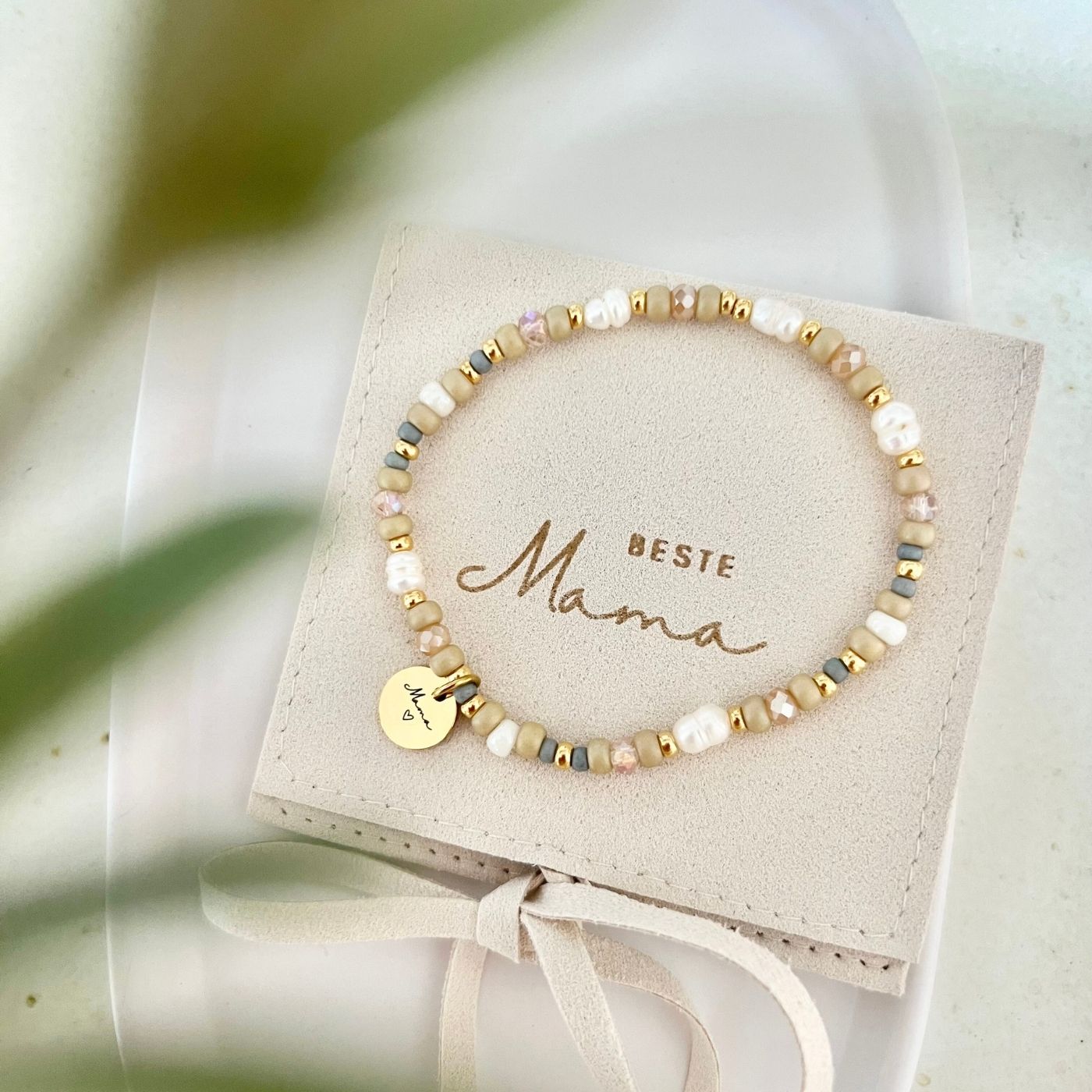 Armband auf Schmuckbeutel mit Aufschrift „Beste Mama“, Perlen in verschiedenen Größen und sanften Naturtönen, dekorativ auf einer Keramikschale präsentiert.