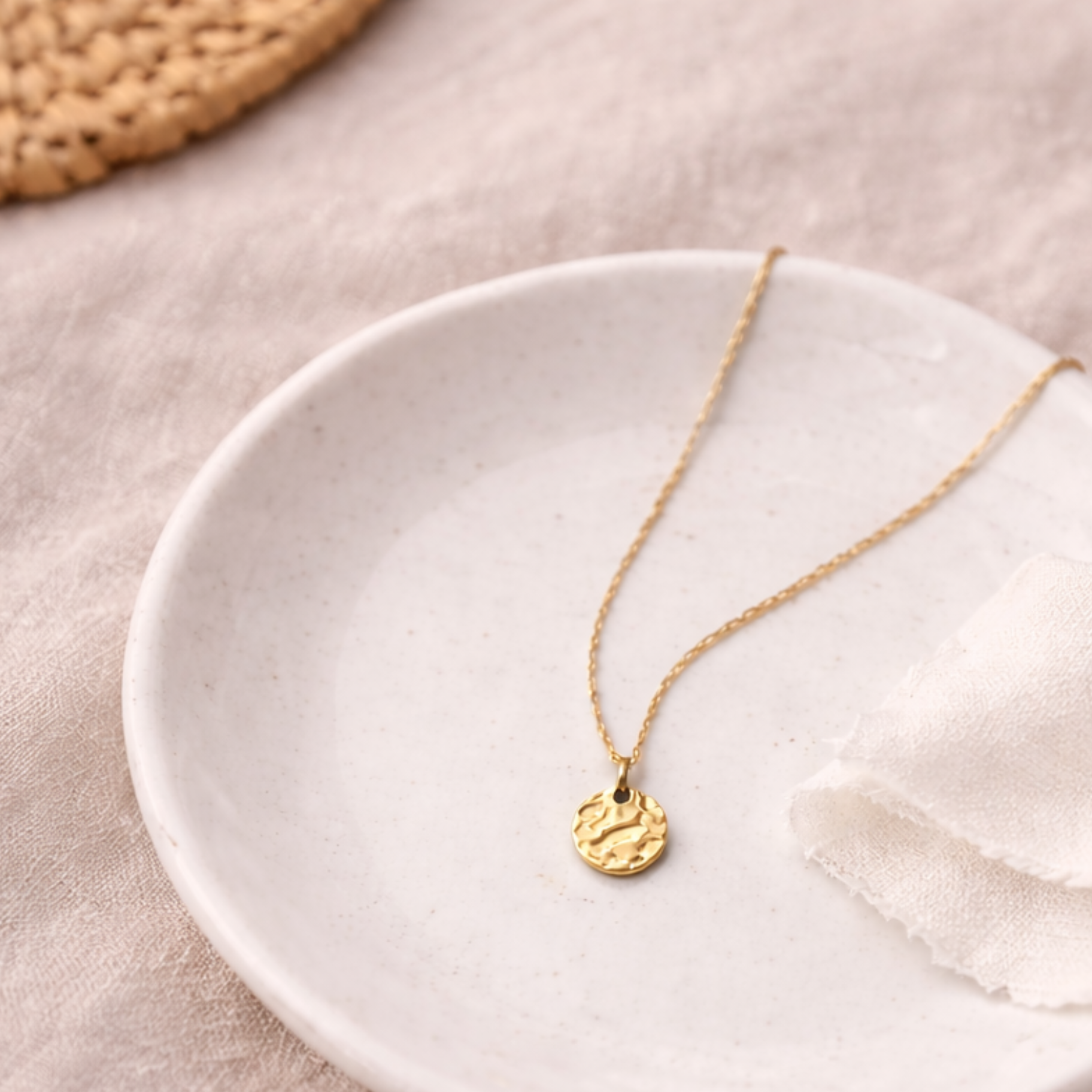 Goldene Edelstahl Halskette mit gehämmertem Anhänger auf weißer Keramikschale und beigem Leinen, minimalistisches Flatlay Schmuck für Frauen