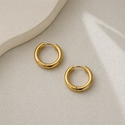 Goldene Huggie Hoops Creolen aus Edelstahl auf hellem Stein, kleine runde Ohrringe, minimalistisch und wasserfest