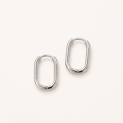 Silberne Huggie Hoops Creolen aus Edelstahl auf hellem Hintergrund, ovale kleine Ohrringe für Damen, wasserfest und minimalistisch