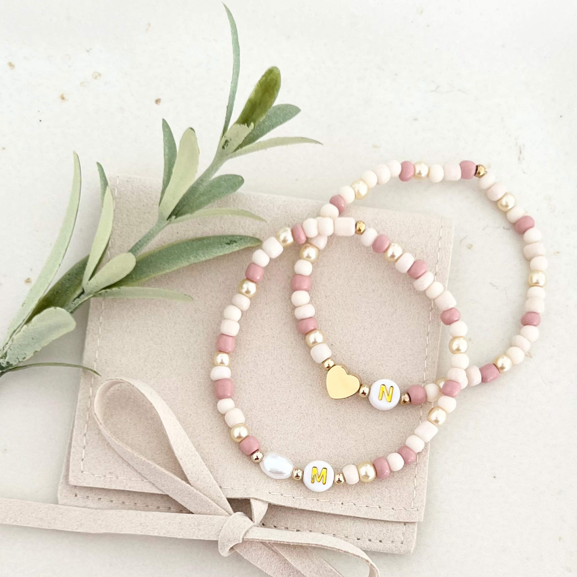 Zwei handgemachte Armbänder aus dem DIY Kit ROSA mit Anhängern „M“ und „N“ – personalisierte Freundschaftsarmbänder für kreative DIY Bastelstunden.
