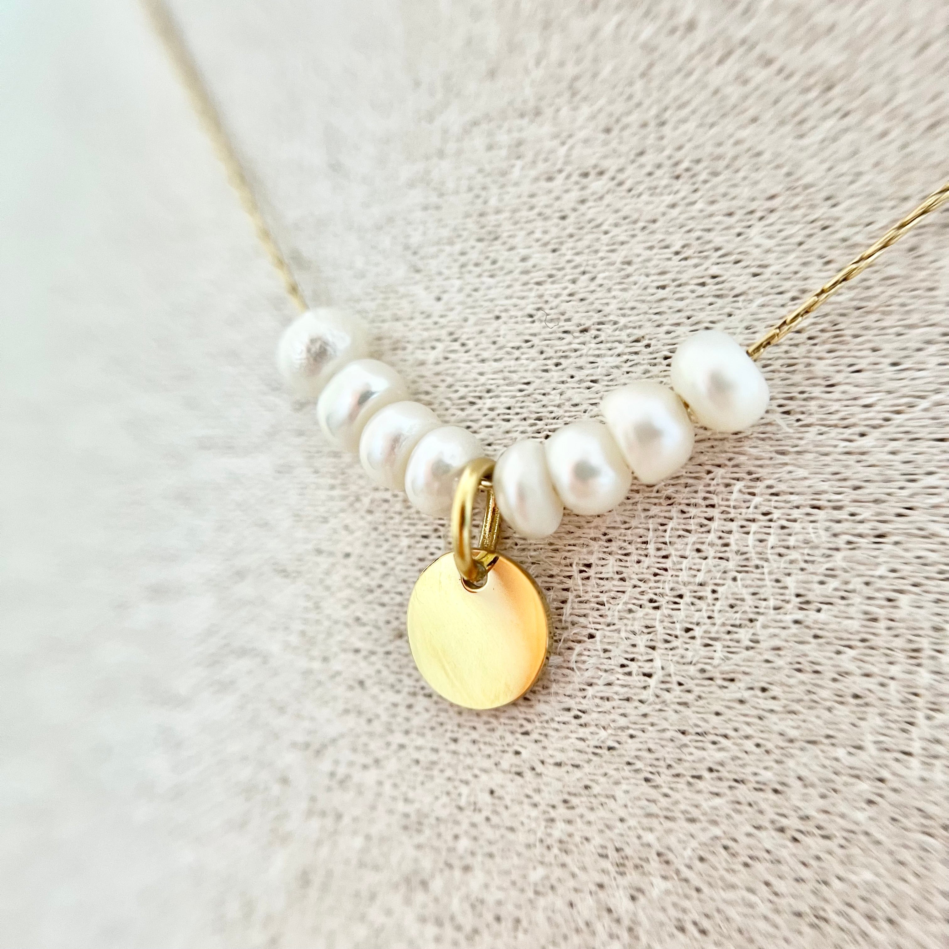 Nahaufnahme der goldenen Kette mit rundem goldenen Anhänger und weißen Süßwasserperlen – minimalistisches Design für luxuriöse Akzente