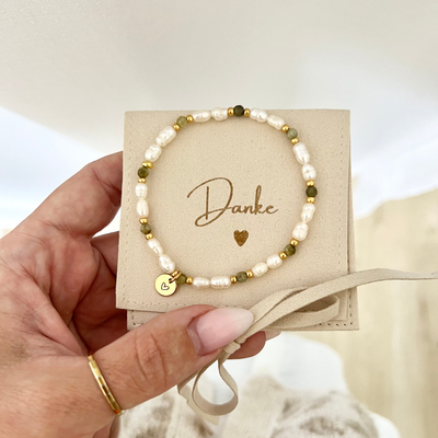 Handgemachtes Armband mit weißen Süßwasserperlen, grünen Natursteinperlen und goldenen Details, präsentiert auf einer Schmucktasche mit „Danke“-Aufschrift. Ein vergoldeter Herzanhänger macht es zum idealen Dankeschön-Geschenk für die Trauzeugin nach der Hochzeit.