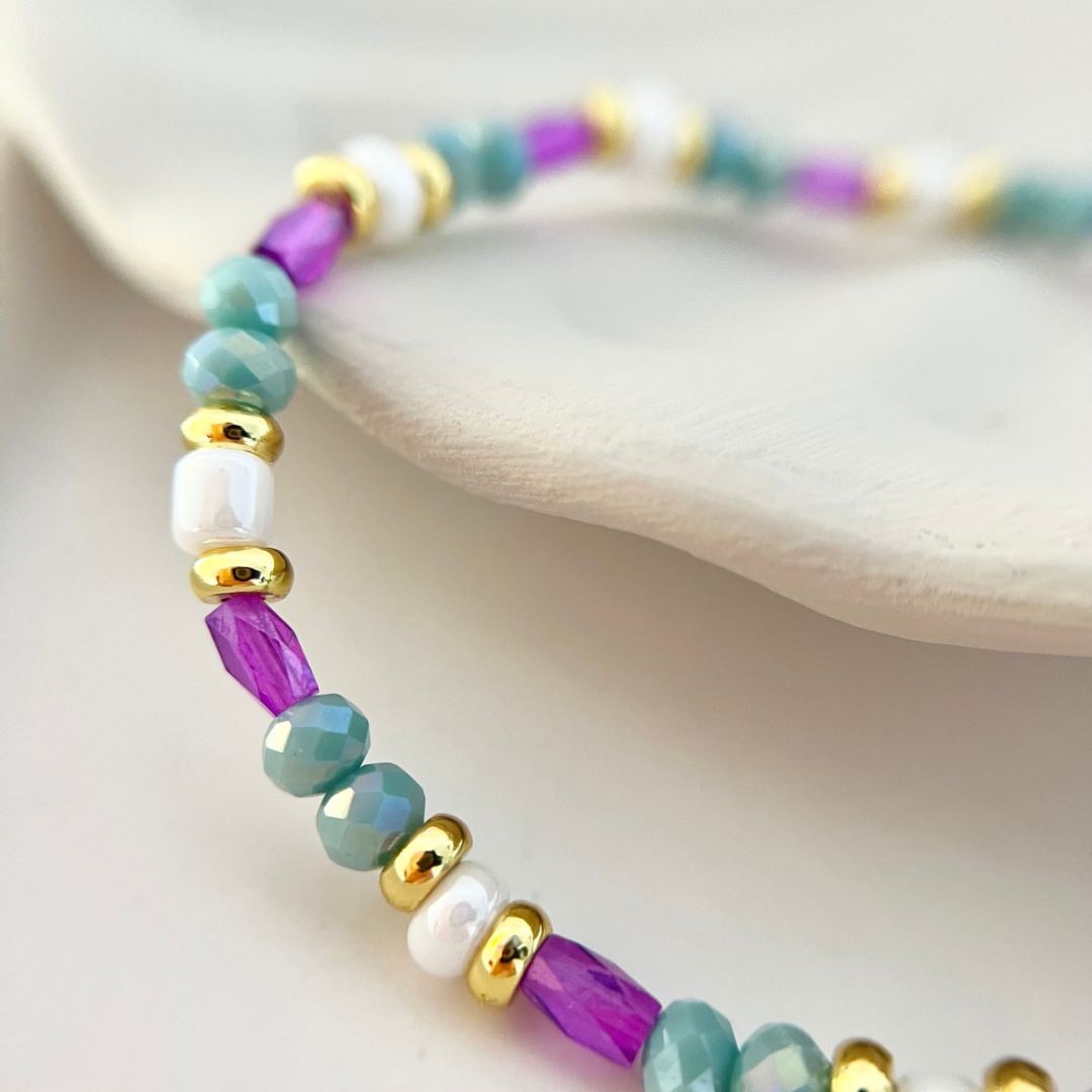 Detailaufnahme der luxuriösen Perlen und goldenen Akzente des Perlenarmbands im orientalischen Stil, mit schimmerndem Türkis und violetten Perlen