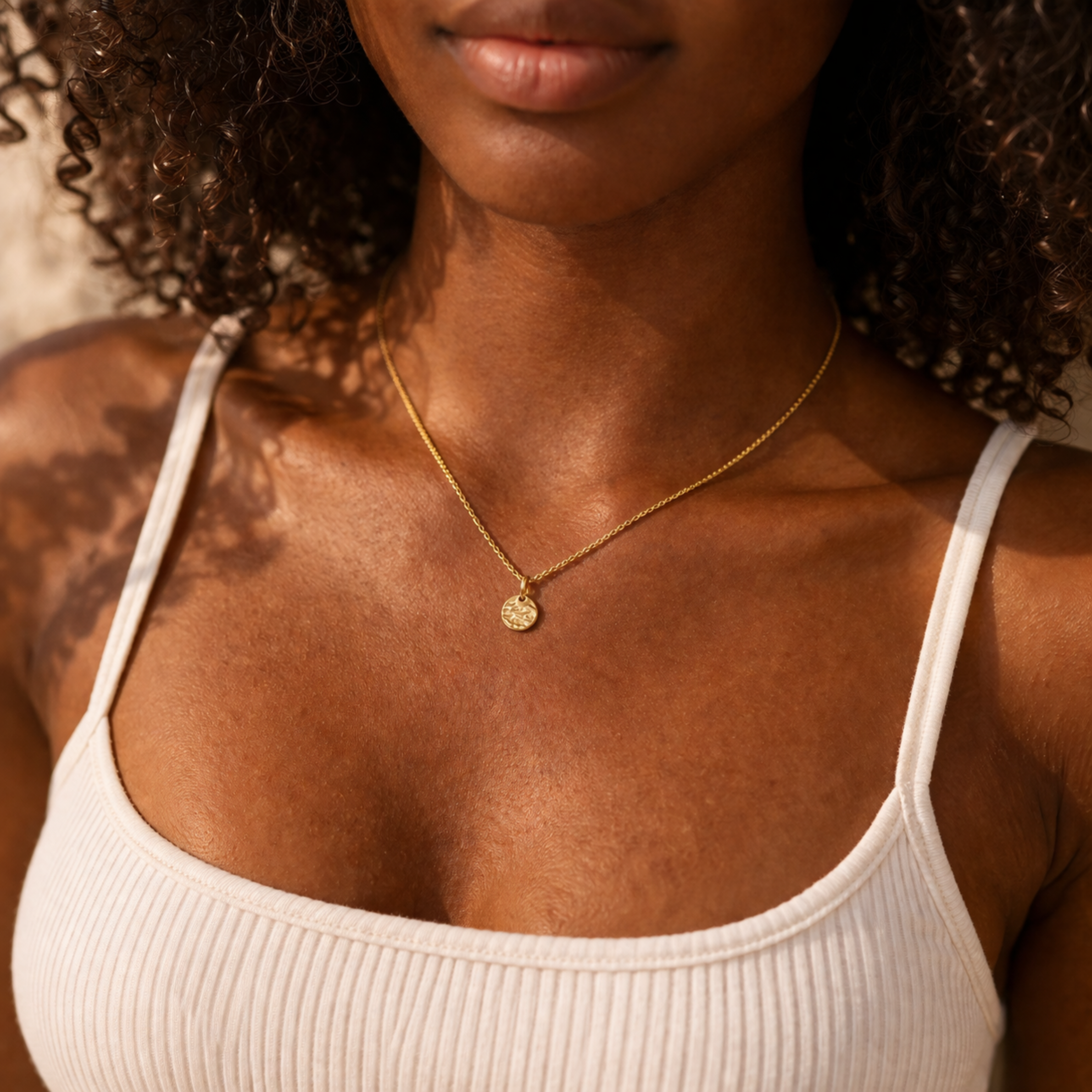 Goldene filigrane Halskette mit kleinem Anhänger getragen von Frau mit dunkler Haut und weißem Crop Top, Fokus auf Dekolleté und Schmuckstück