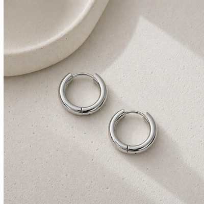 Silberne Huggie Hoops Creolen aus Edelstahl auf hellem Stein, kleine runde Ohrringe, minimalistisch und wasserfest