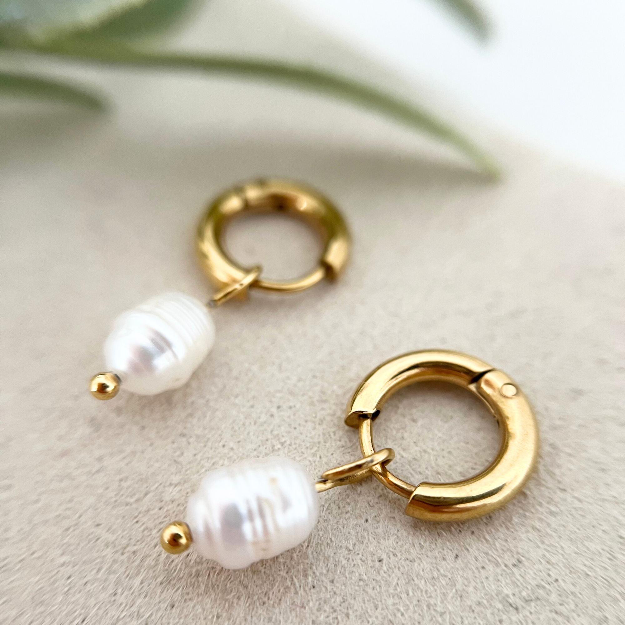 Detailaufnahme eines goldenen Edelstahl-Ohrrings ISLA mit Süßwasserzuchtperle, die den minimalistischen und eleganten Stil betont.